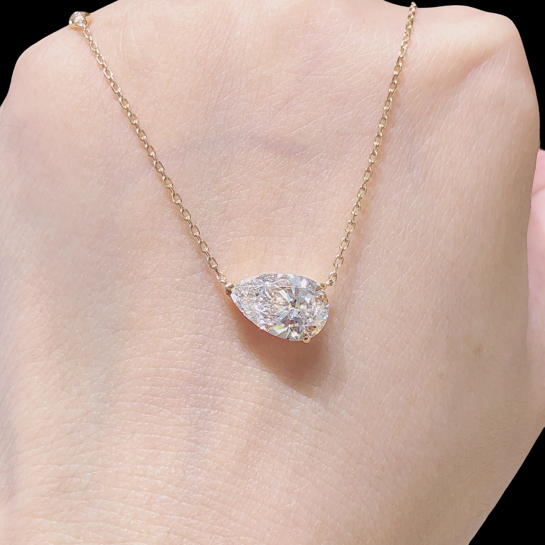 Gold necklace with a pear-shaped diamond pendant on a person's neck.