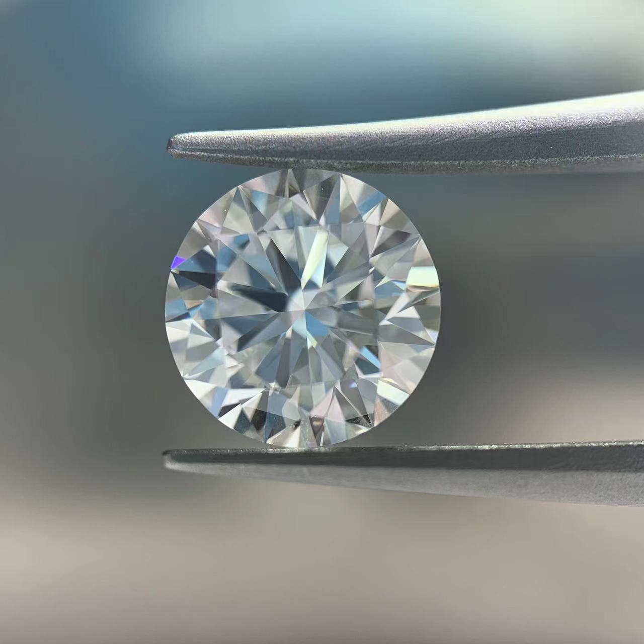 Round diamond held between tweezers against a neutral background