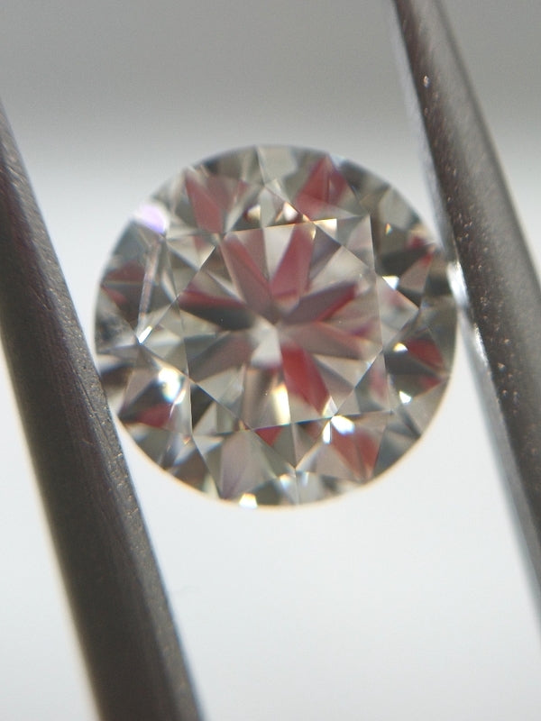 Close-up of a round diamond held between two tweezers on a light gray background