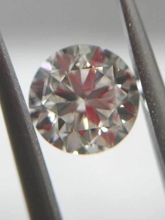 Close-up of a round diamond held between two tweezers on a light gray background