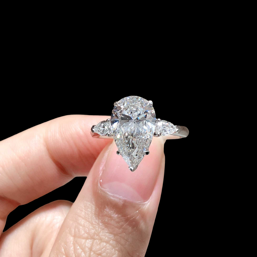 Diamond ring held between fingers against a black background