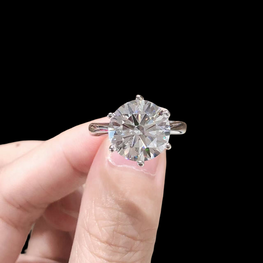 Diamond ring held between fingers against a black background