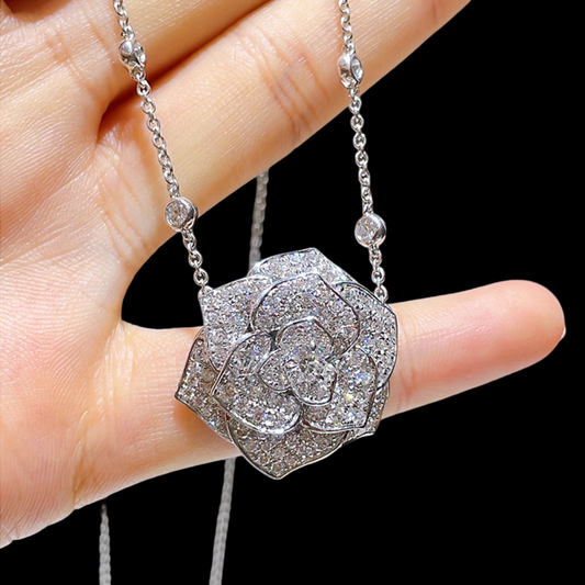 Silver necklace with a diamond-encrusted pendant held by a hand against a black background