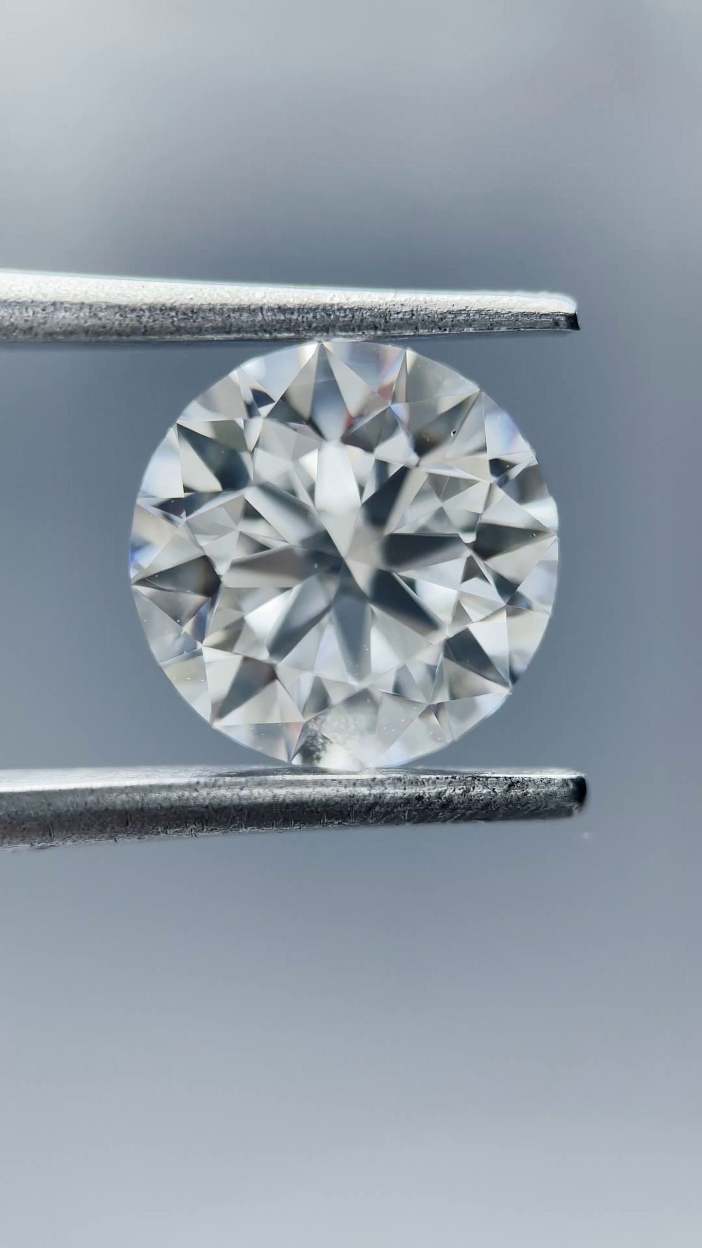 Round diamond held between tweezers against a neutral background