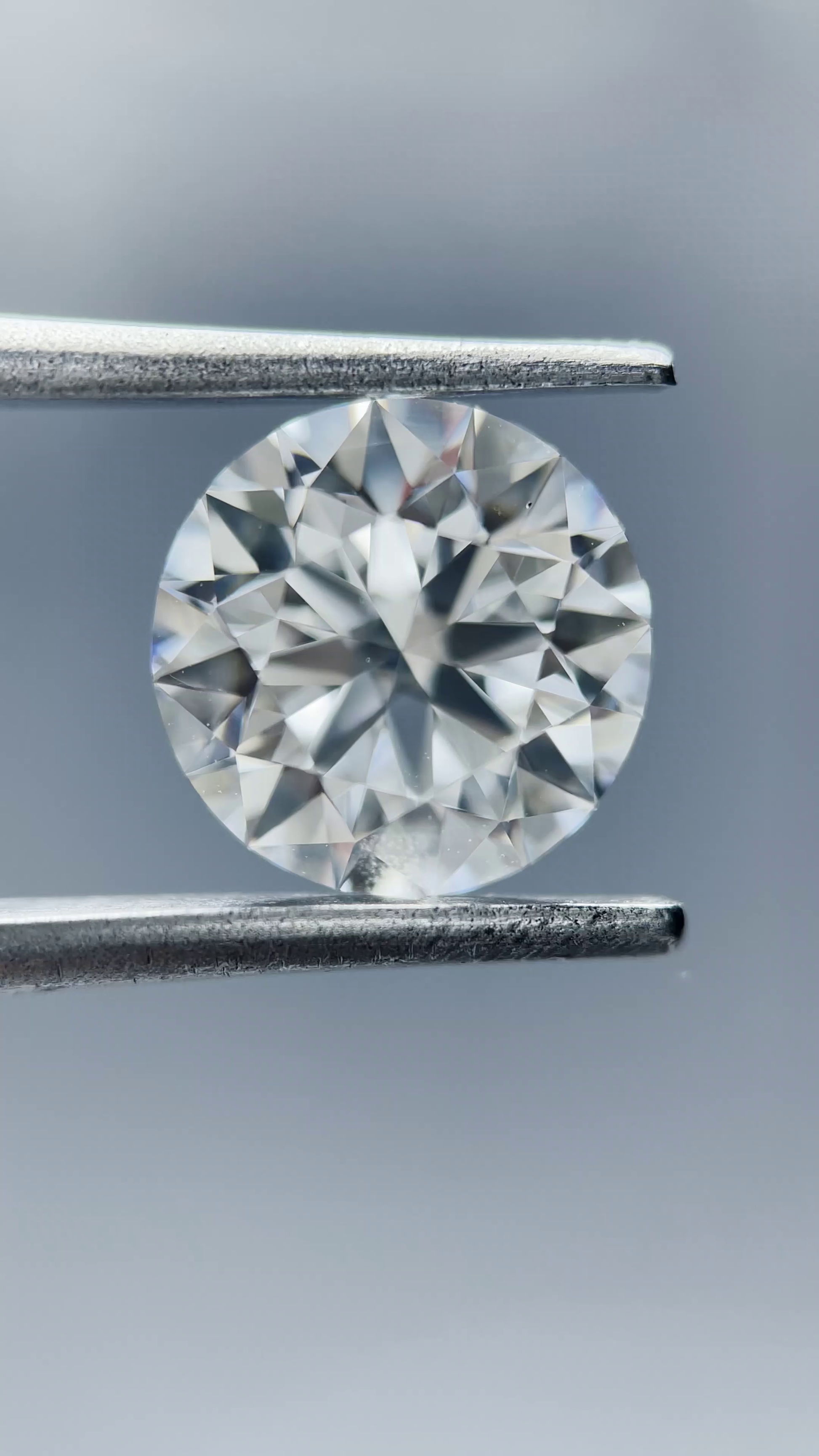 Round diamond held between tweezers against a neutral background