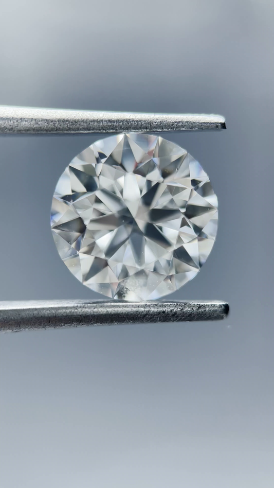 Round diamond held between tweezers against a neutral background