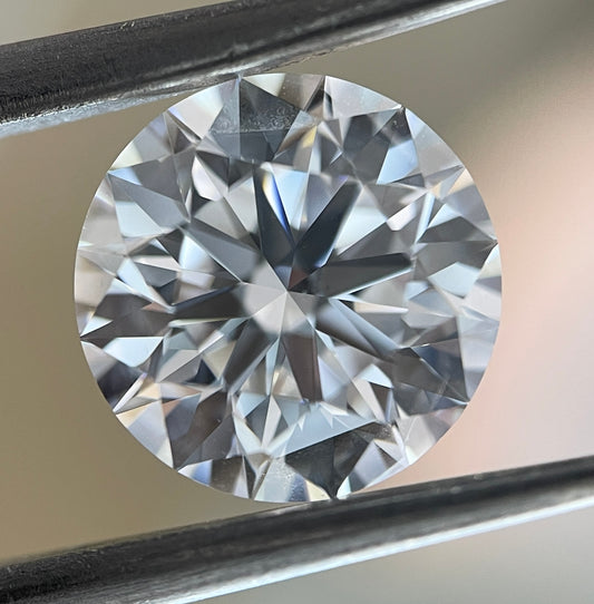 Close-up of a round diamond held by tweezers against a neutral background