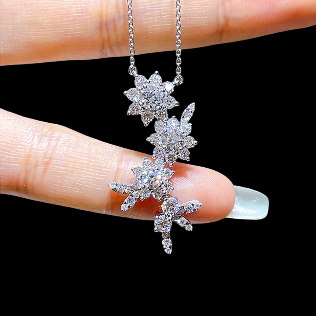 Silver floral necklace held between fingers against a black background