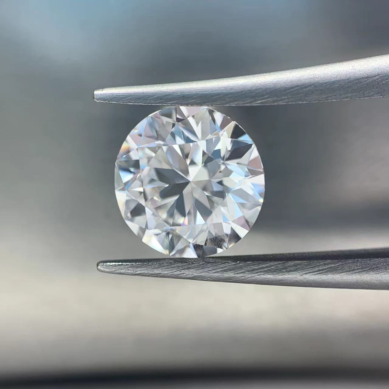 Round diamond held between tweezers against a neutral background
