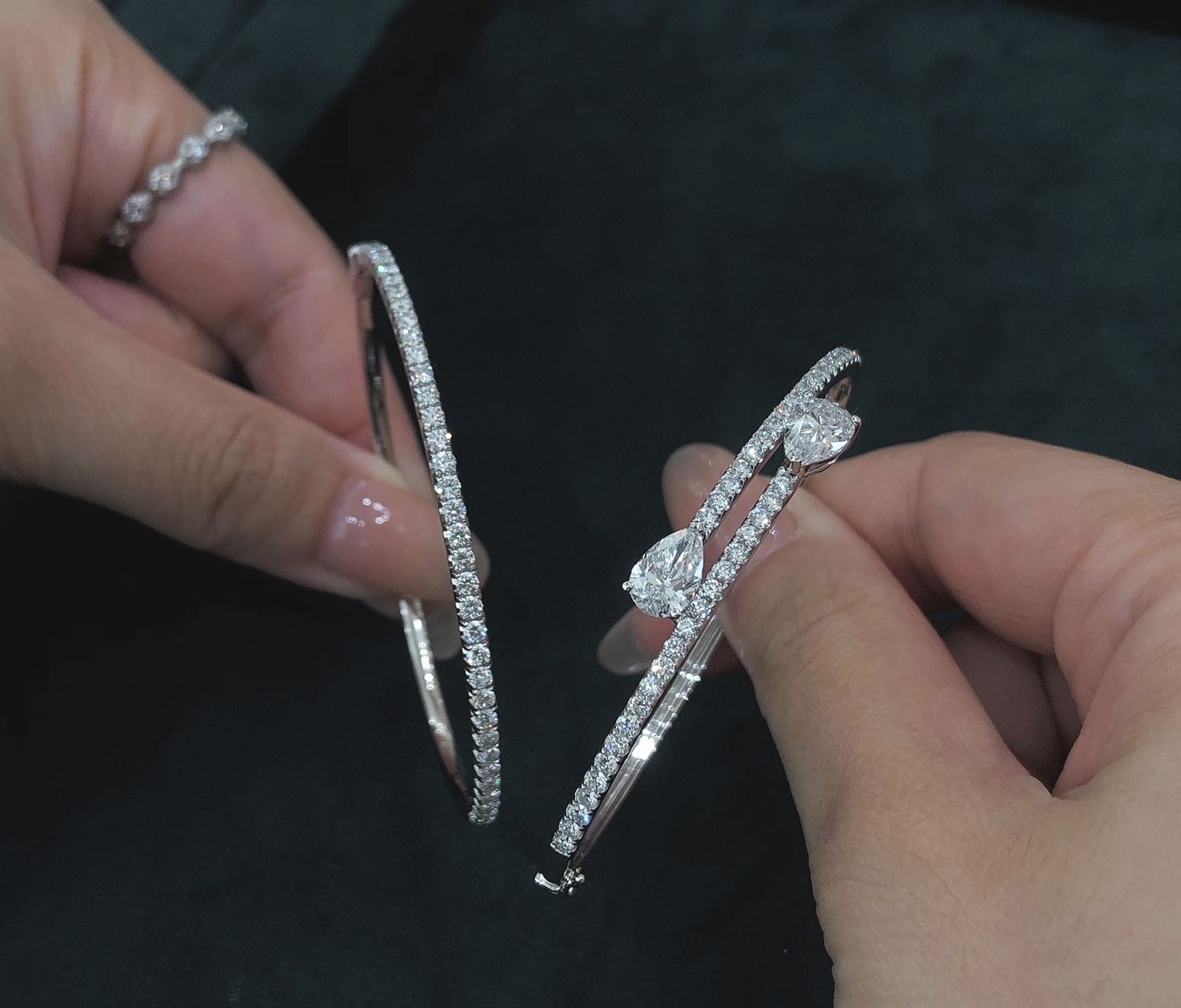 Two silver bracelets with diamond accents held by hands against a dark background