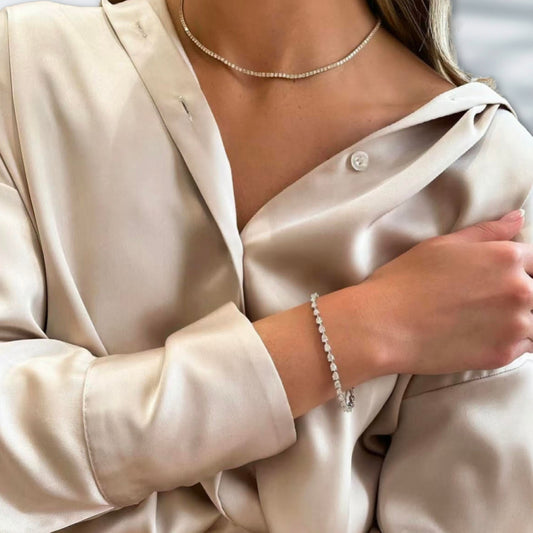 Close-up of a person wearing a beige satin shirt with a bracelet and necklace.